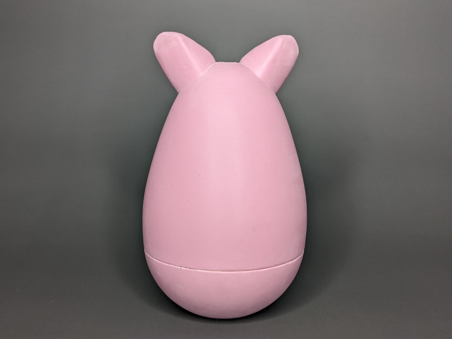 The back-side of the Kalua the Peeg tama. It is a pink egg-shaped 3d-printed tama with ears sticking out of the top of the egg shape. A seam sits just below the widest point of the tama.