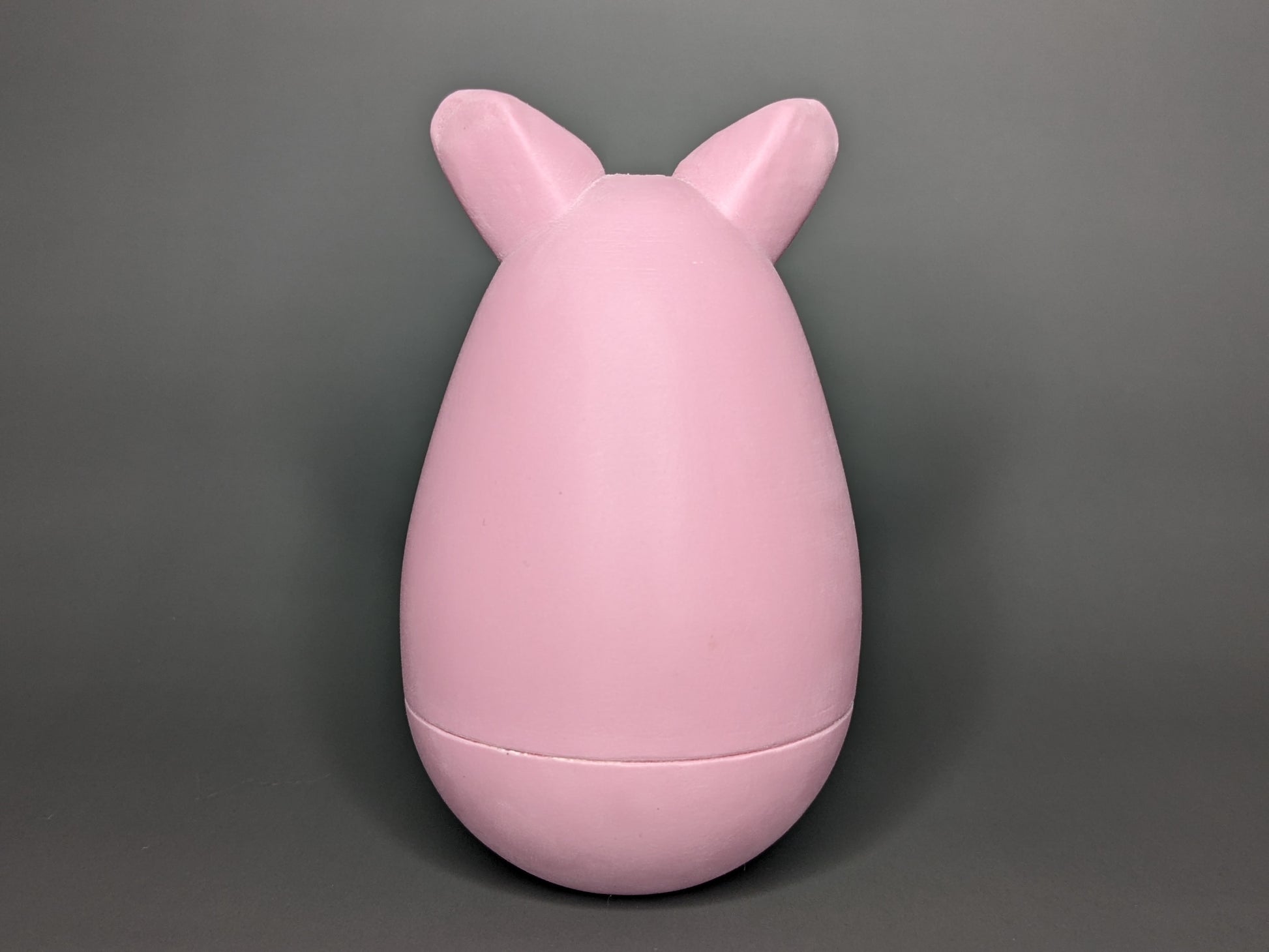 The back-side of the Kalua the Peeg tama. It is a pink egg-shaped 3d-printed tama with ears sticking out of the top of the egg shape. A seam sits just below the widest point of the tama.